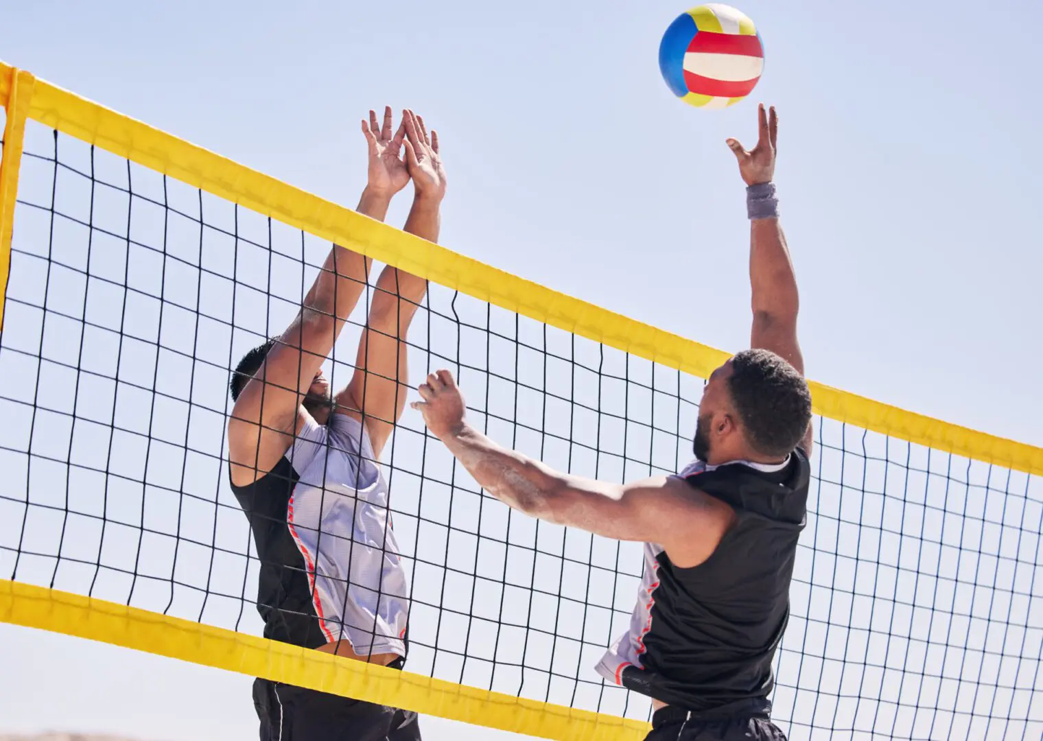 Two men playing beach volleyball with a colorful ball.